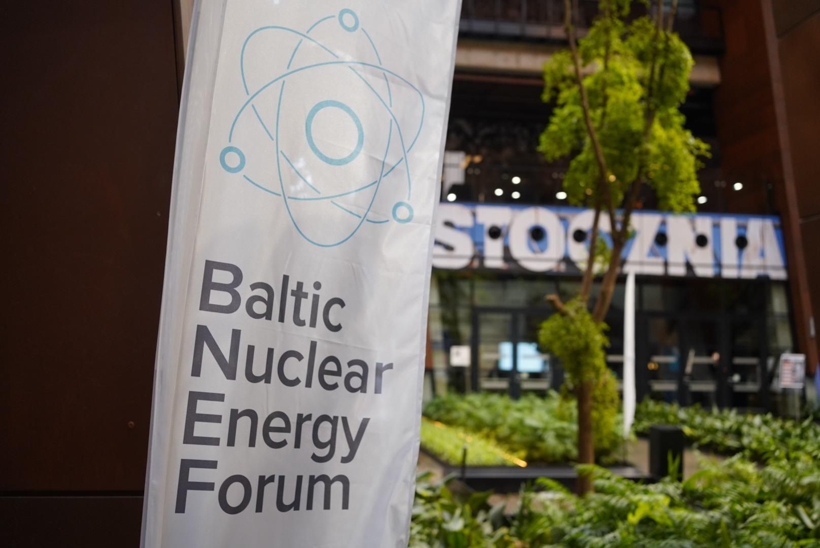 Zdjęcie flagi z nazwą Baltic Nuclear Energy Forum, a w tle zieleń i napis STOCZNIA